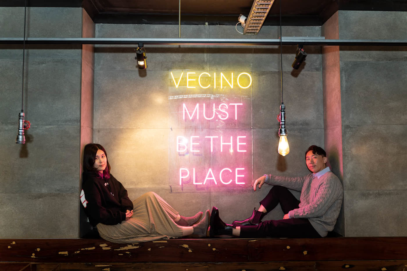 Tony and co-founder Eunice under the VECINO Must Be The Place neon sign